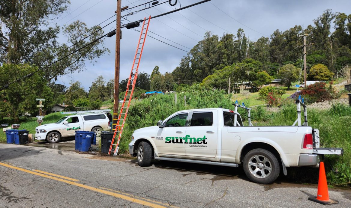 Two surfnet trucks parked near an electrical line with a ladder reaching up to the line